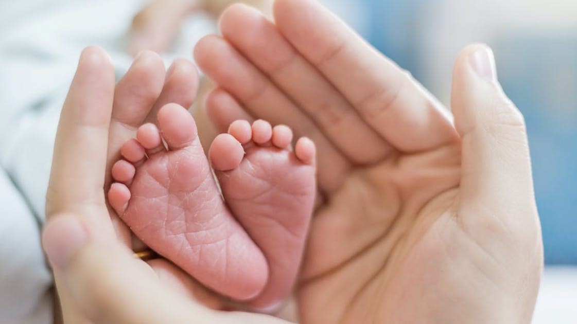 Des petits pieds de bébé dans des mains adulte